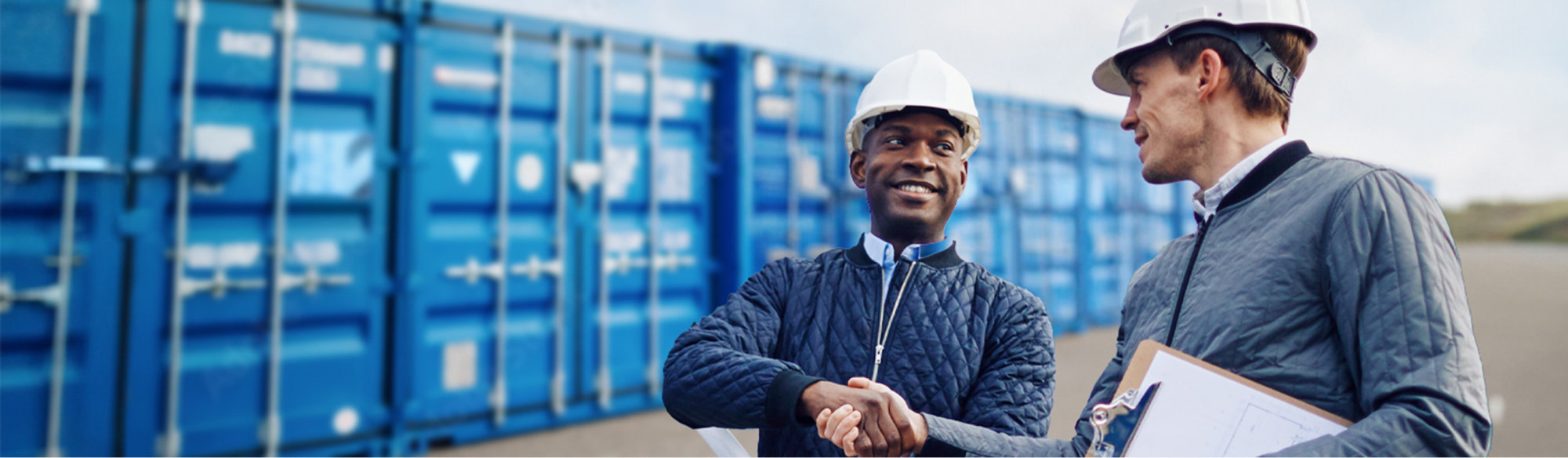 Two men shaking hands in front of storage containers