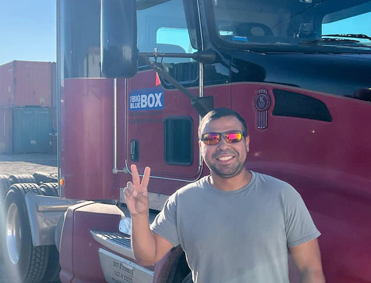 A man smiling in front of a Big Blue Box semi truck