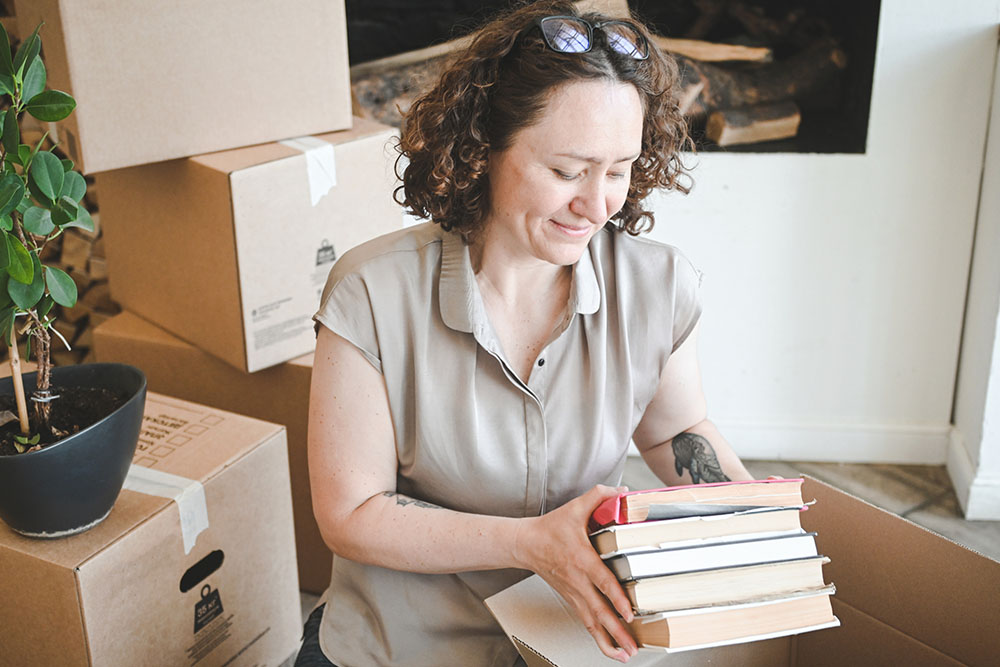 A woman holding books surrounded by moving boxes